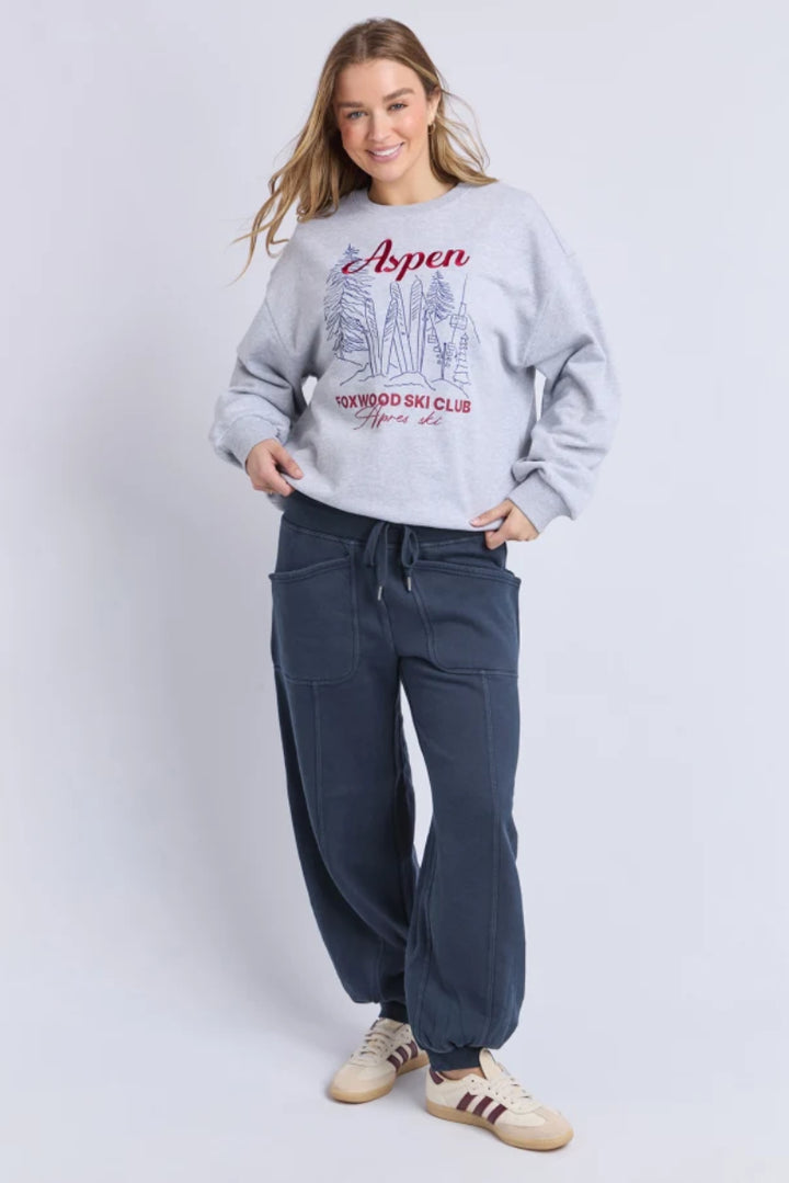 Person wearing a gray sweatshirt with 'Aspen' text and blue pants on a white background