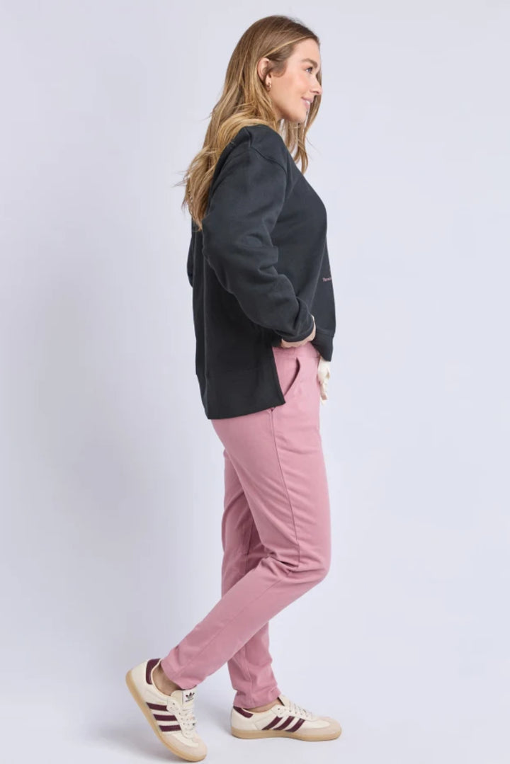 Woman wearing a black jacket and pink pants on a light gray background
