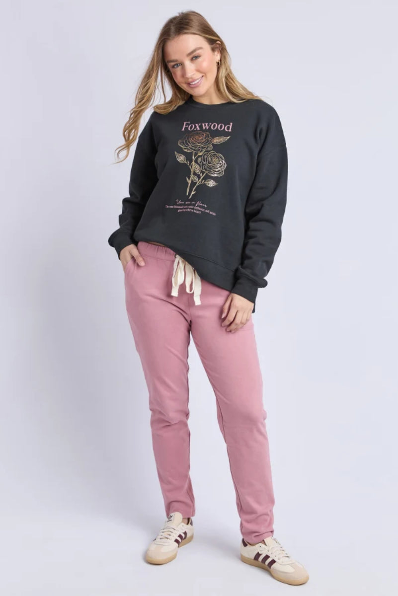 Woman wearing a black sweatshirt with 'Foxwood' text and pink pants on a light gray background