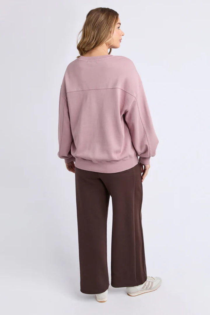 Woman wearing a pink sweater and brown pants on a white background