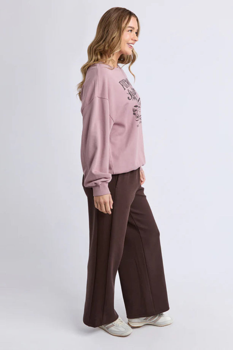 Woman wearing a pink sweatshirt and brown pants on a white background