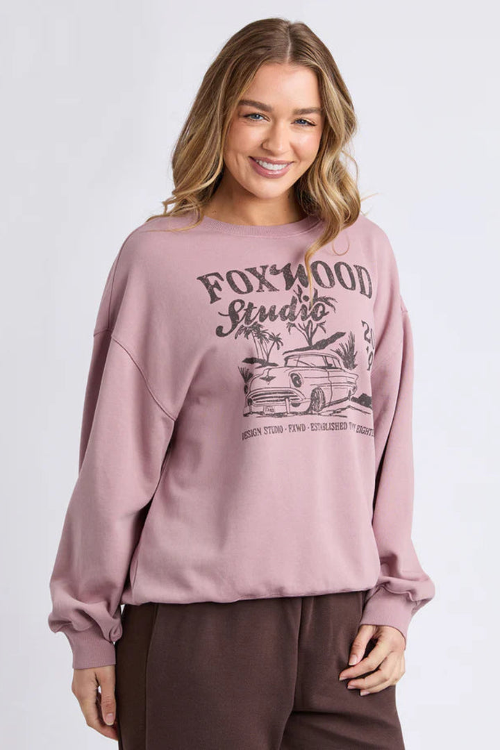 Woman wearing a pink sweatshirt with 'Foxwood Studio' graphic on a white background