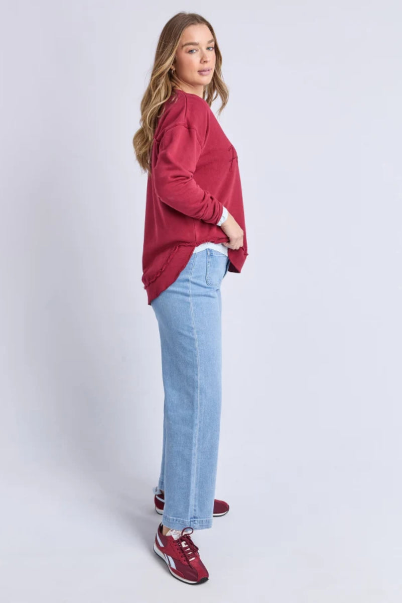 Woman wearing a red sweater and light blue jeans on a white background