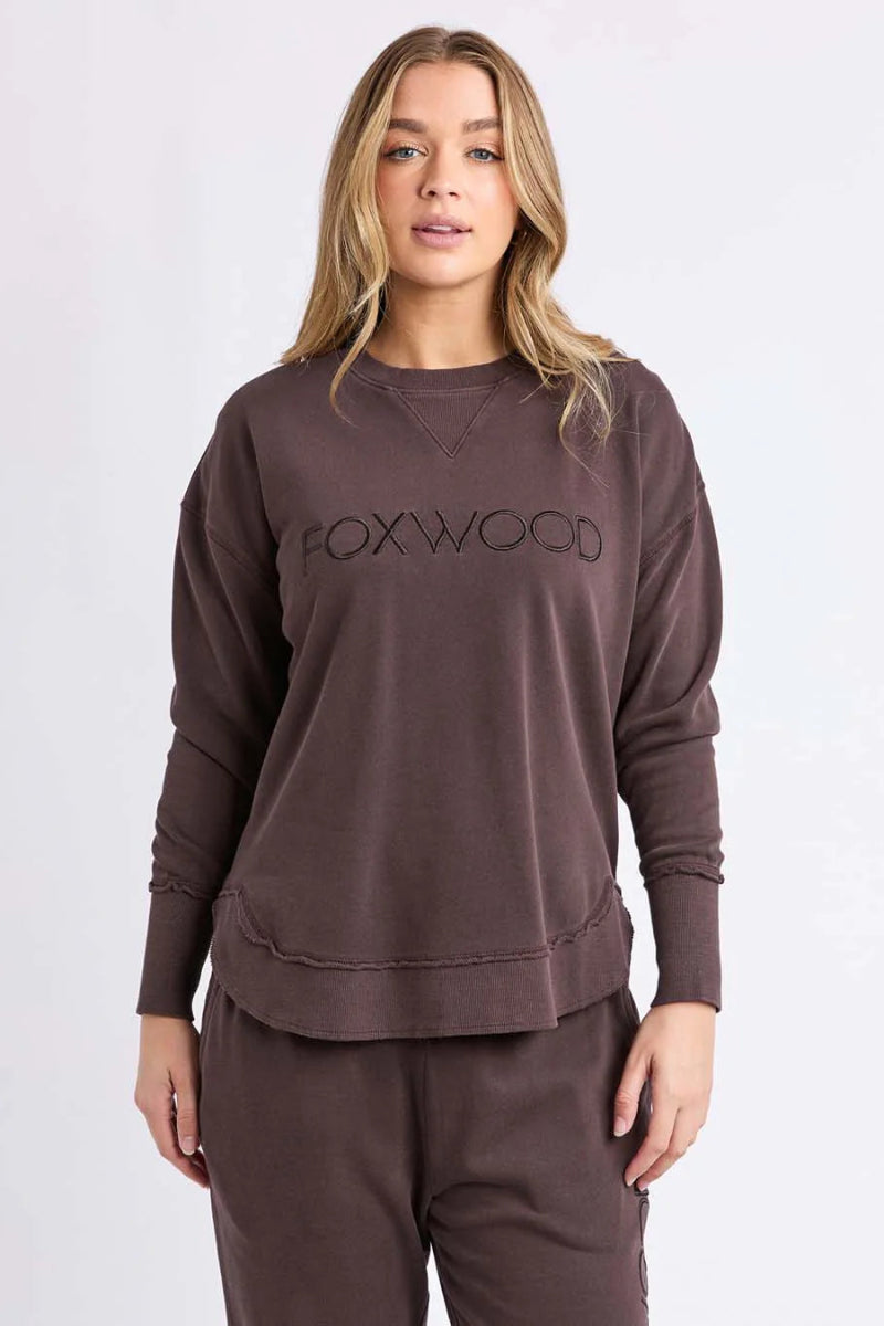 Woman wearing a brown sweatshirt with 'FOXWOOD' logo on a white background
