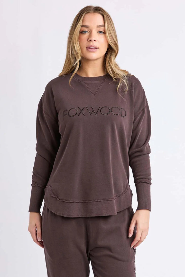 Woman wearing a brown sweatshirt with 'FOXWOOD' logo on a white background