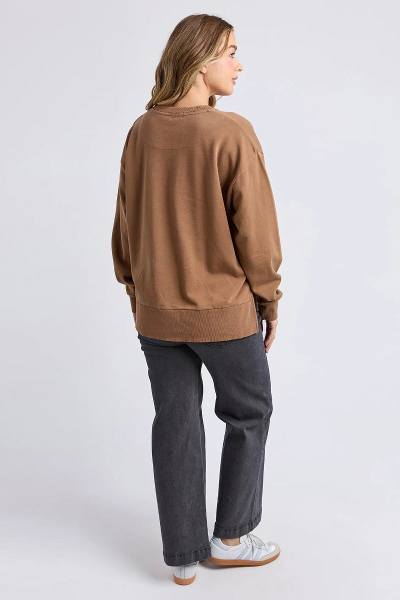 Person wearing a brown sweater and dark pants on a white background