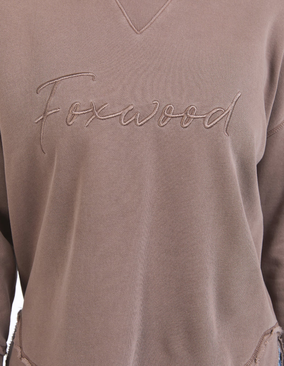 Close-up of brown Foxwood sweatshirt with embroidered logo and ribbed neckline.