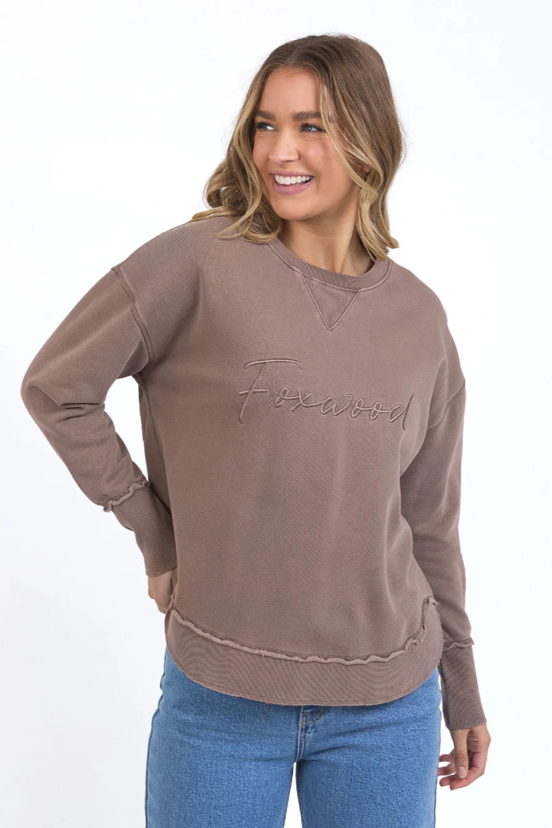 Woman wearing a brown sweatshirt with 'Flawless' embroidery on a white background