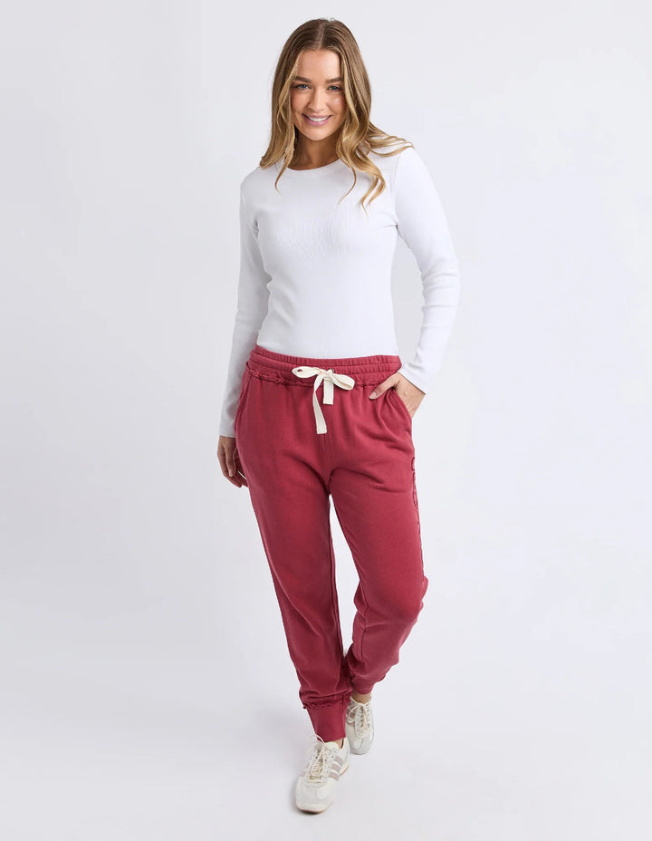 Woman wearing rust Foxwood track pants, white long-sleeve top, and sneakers.