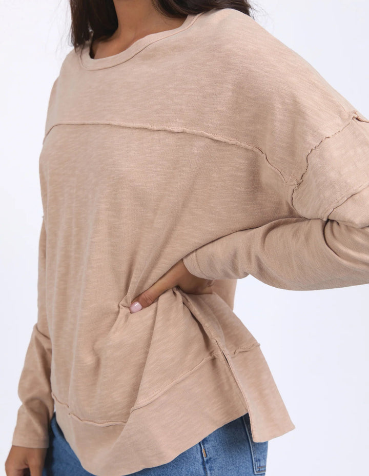 Close-up of women wearing long-sleeve top in oat color with relaxed fit and seam details.
