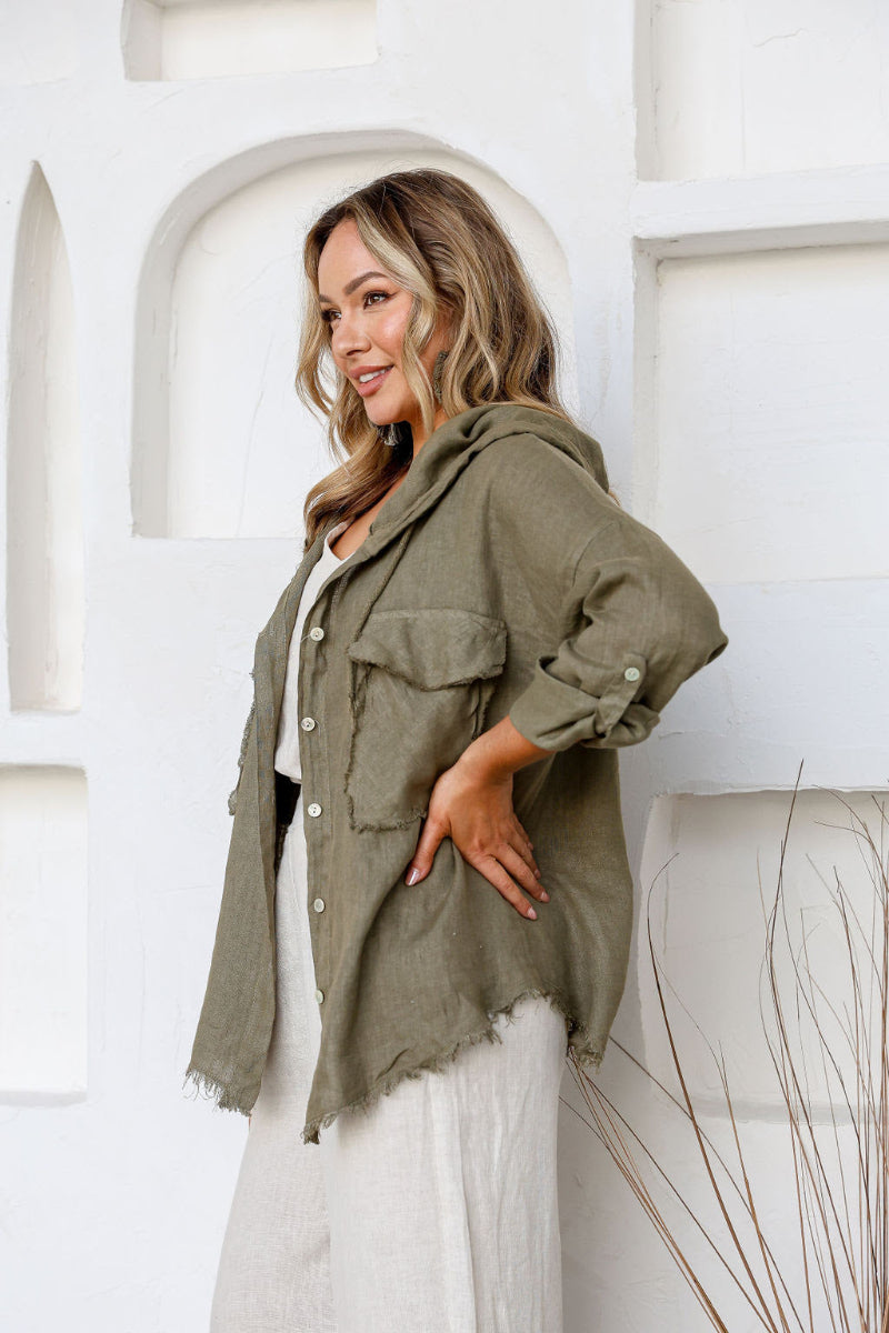 Woman wearing a green jacket standing against a white wall.