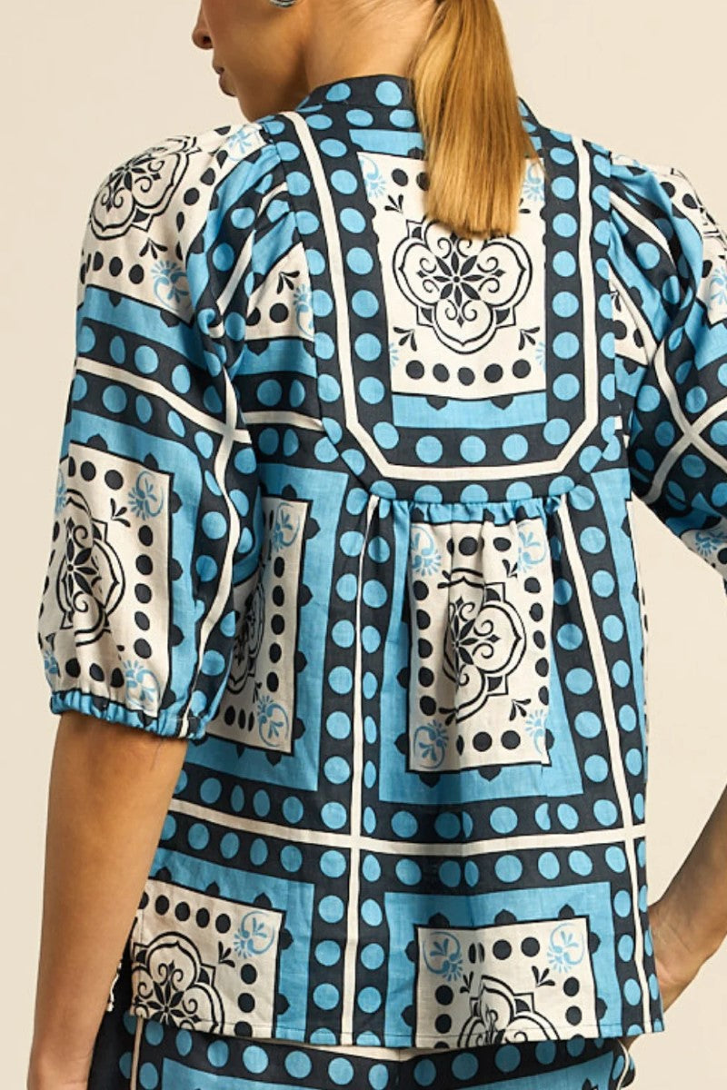 Person wearing a blue patterned blouse with a neutral background