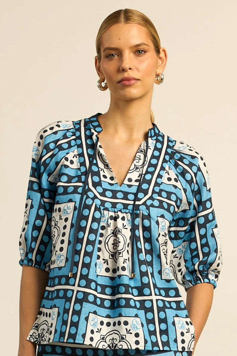 Woman wearing a blue patterned blouse against a beige background