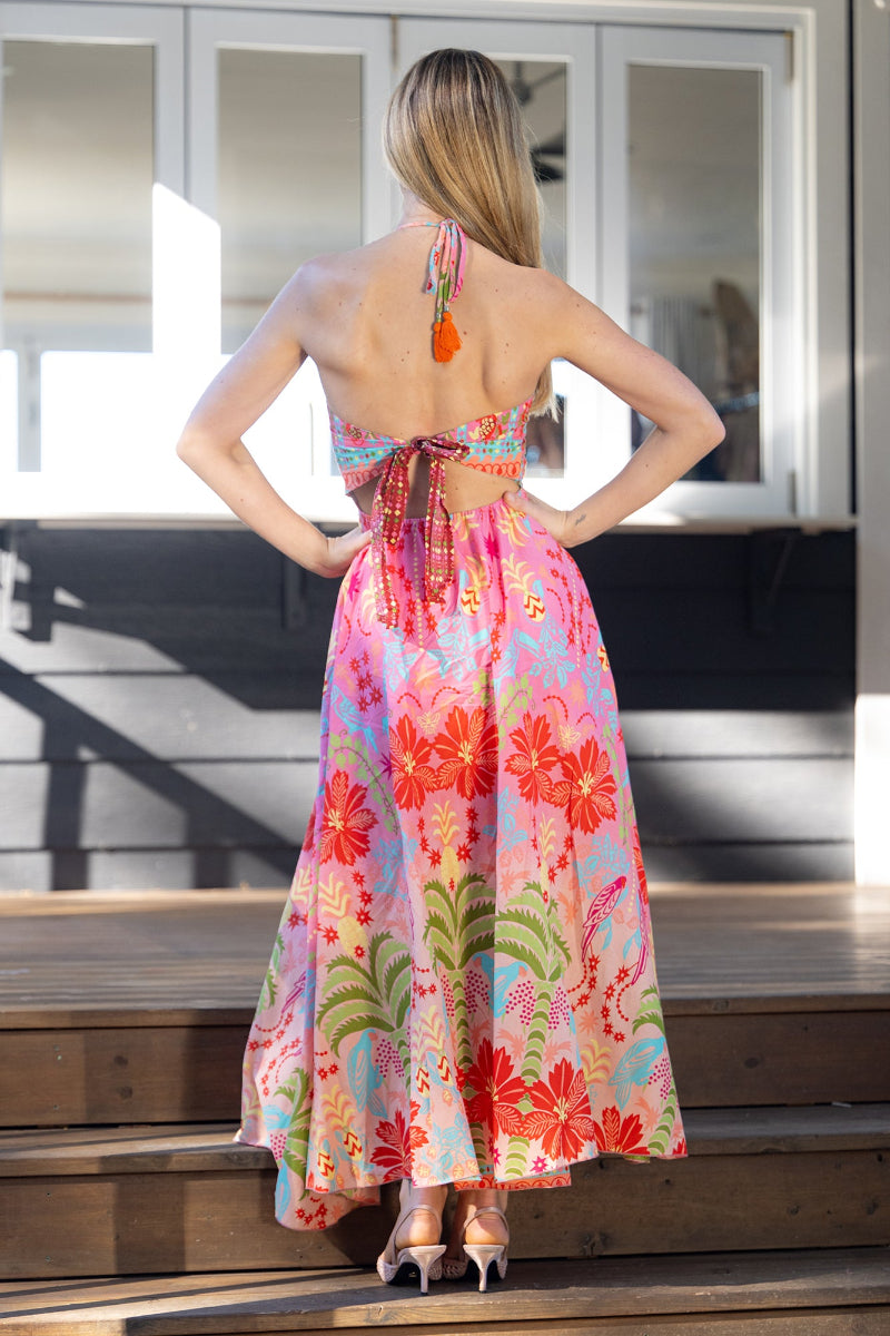 Woman wearing a colorful floral midi/maxi dress on wooden steps. The dress features a halter neck style and flowy skirt, with adjustable tie-up details on the back
