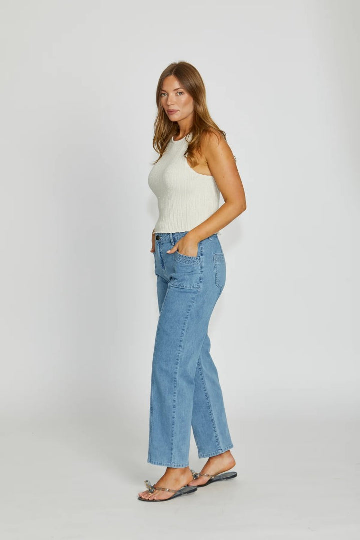 Woman wearing a white sleeveless top and light blue jeans on a white background