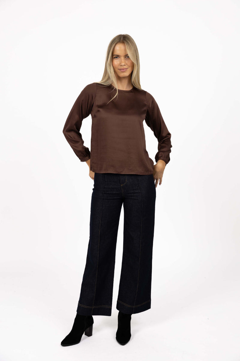 Woman wearing a brown top and black pants on a white background
