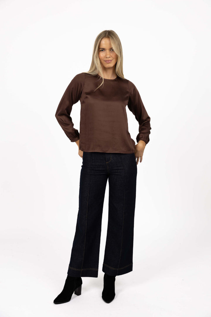 Woman wearing a brown top and black pants on a white background