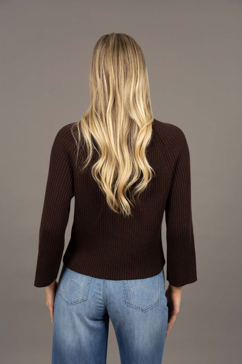 Person wearing a brown ribbed sweater and blue jeans against a gray background