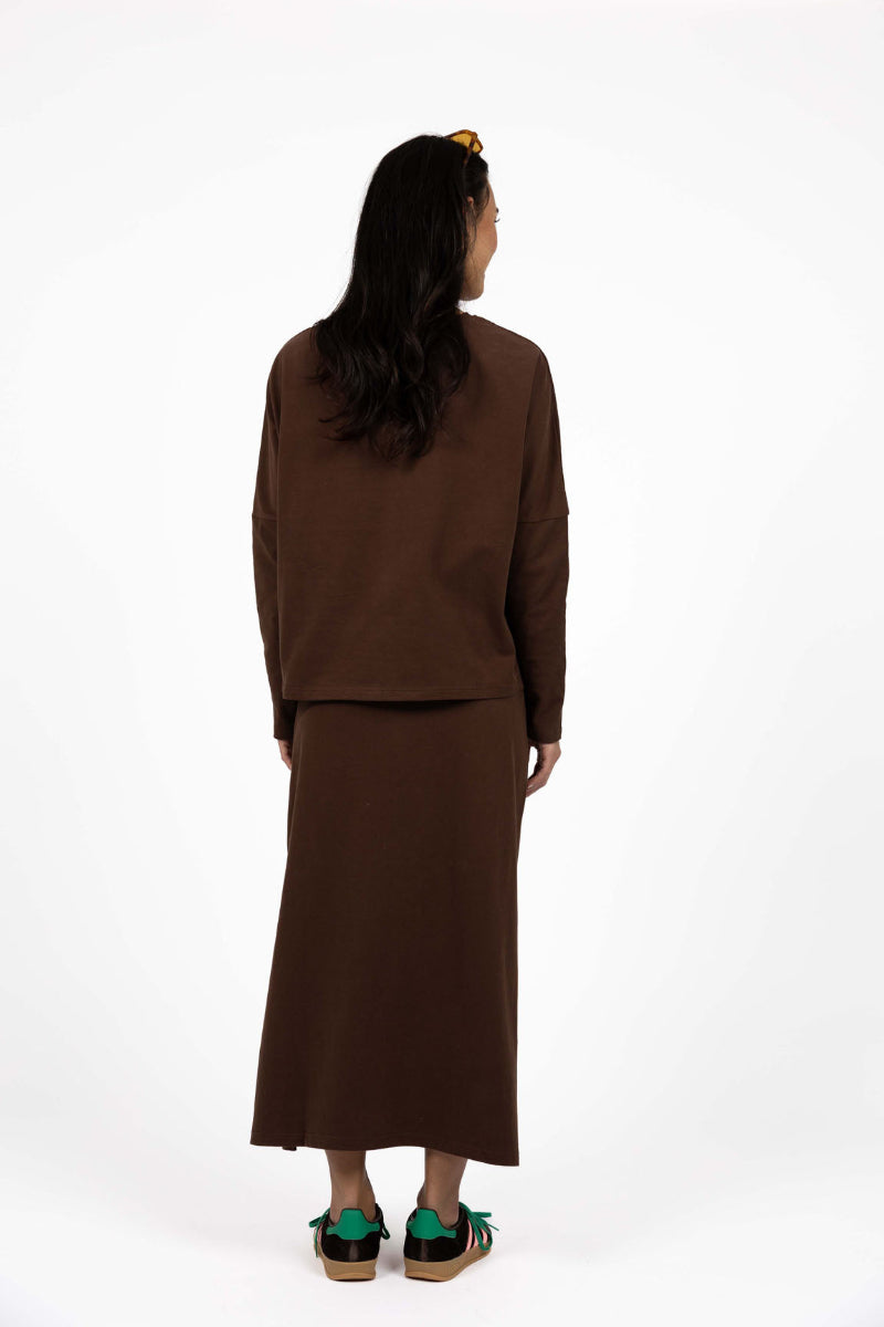 Person wearing a brown outfit with green shoes on a white background