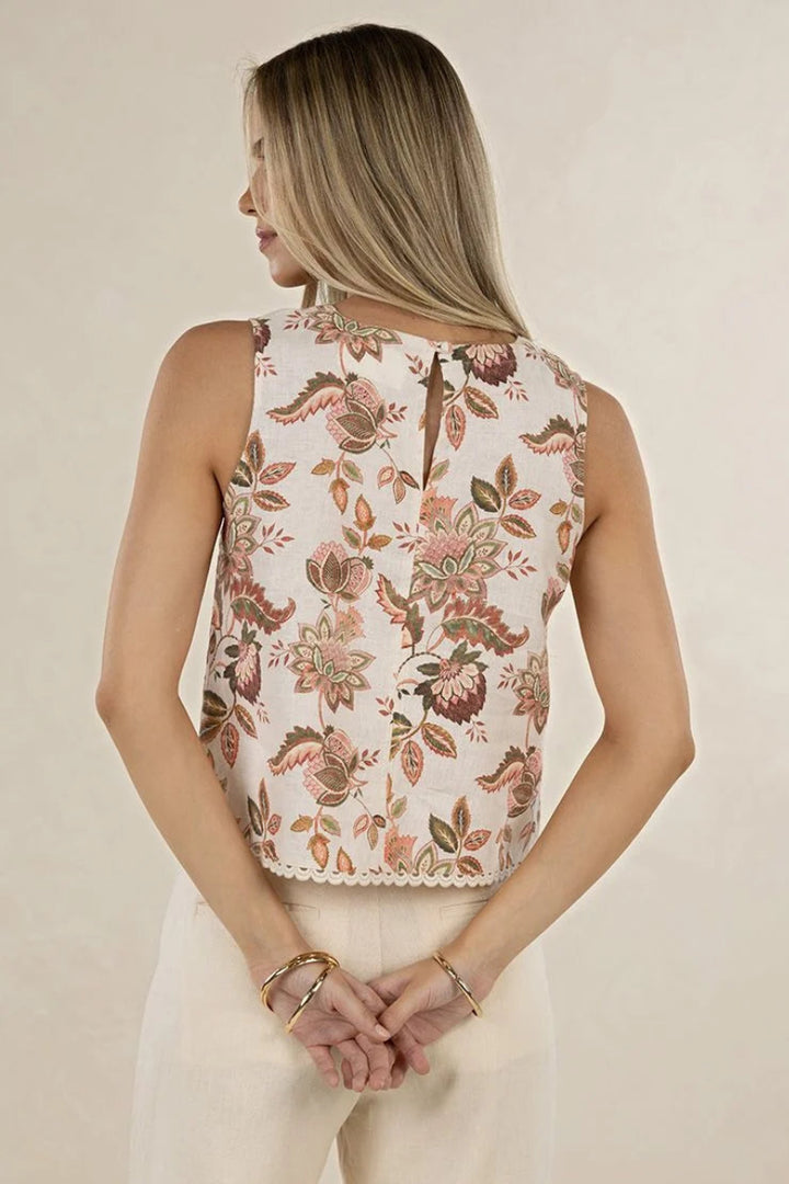 A woman shown from the back wearing a sleeveless cream top with a brown and pink floral pattern and a keyhole back detail, paired with cream pants against a light beige background.
