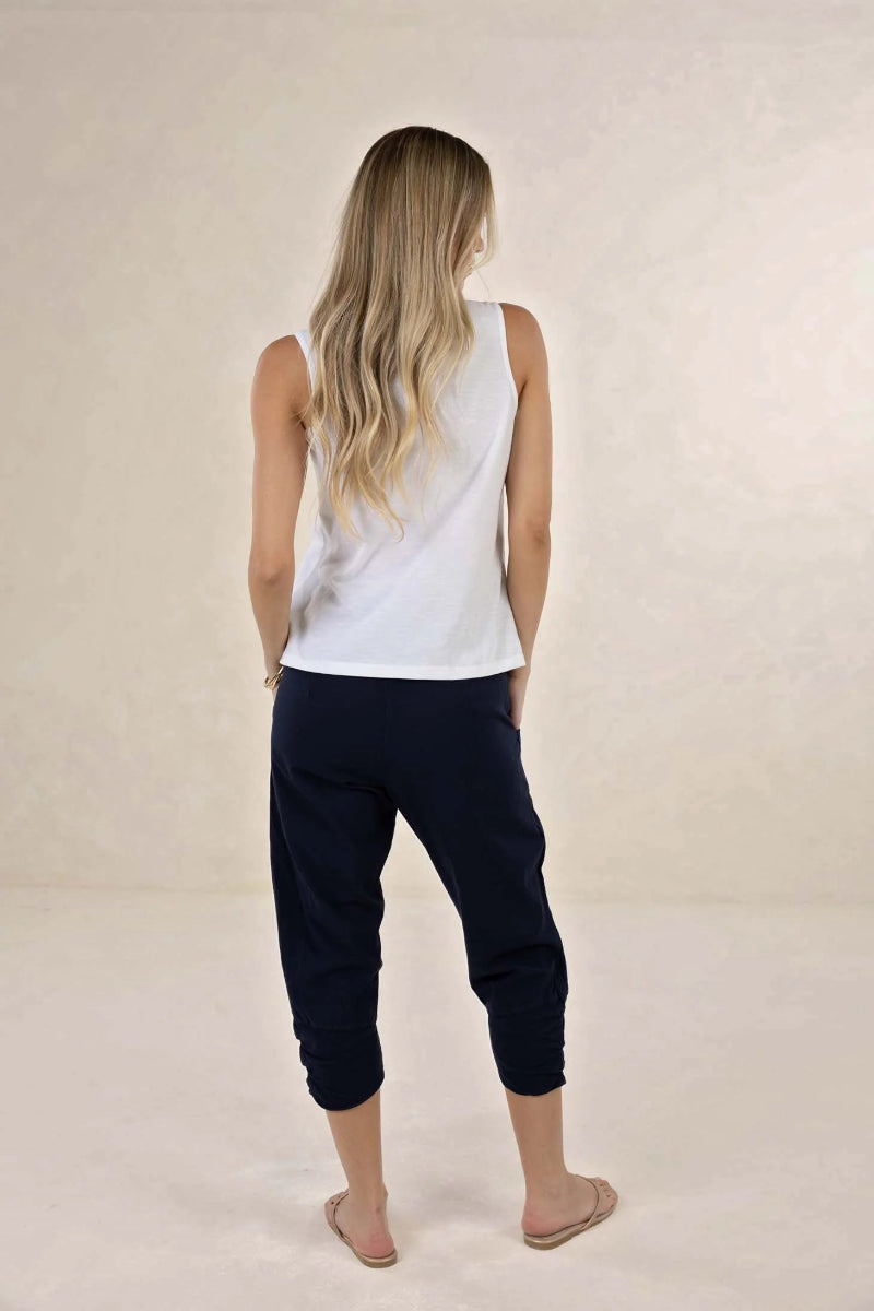 Woman wearing a white sleeveless top and navy pants on a beige background