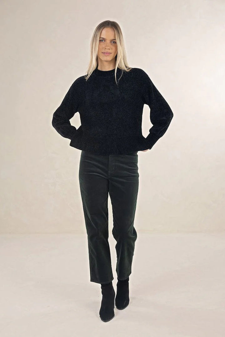 Person wearing a black sweater and dark green pants on a plain background