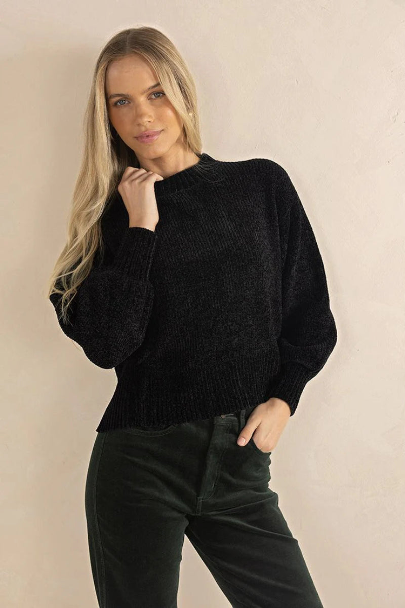 Woman wearing a black sweater and dark pants against a beige background