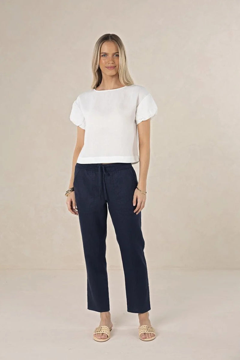 Woman wearing a white top and navy pants on a beige background
