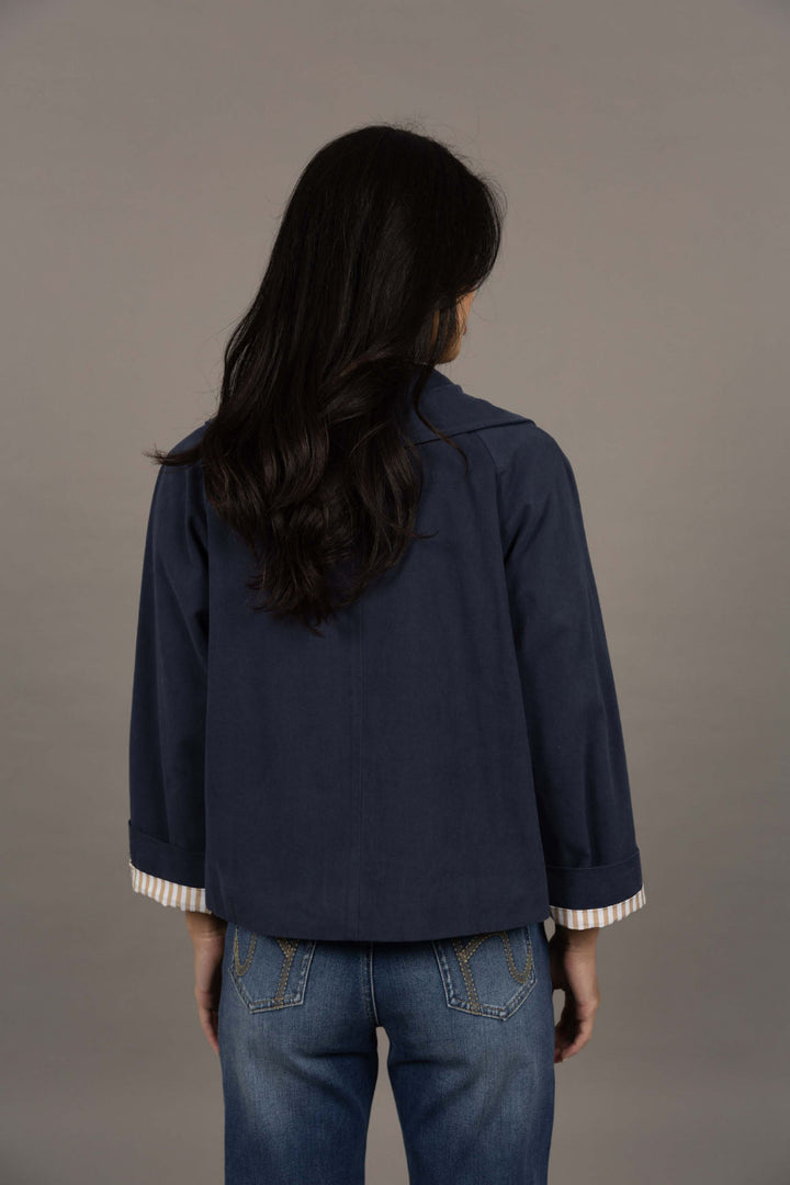 Person wearing a navy blue jacket with white trim on a gray background