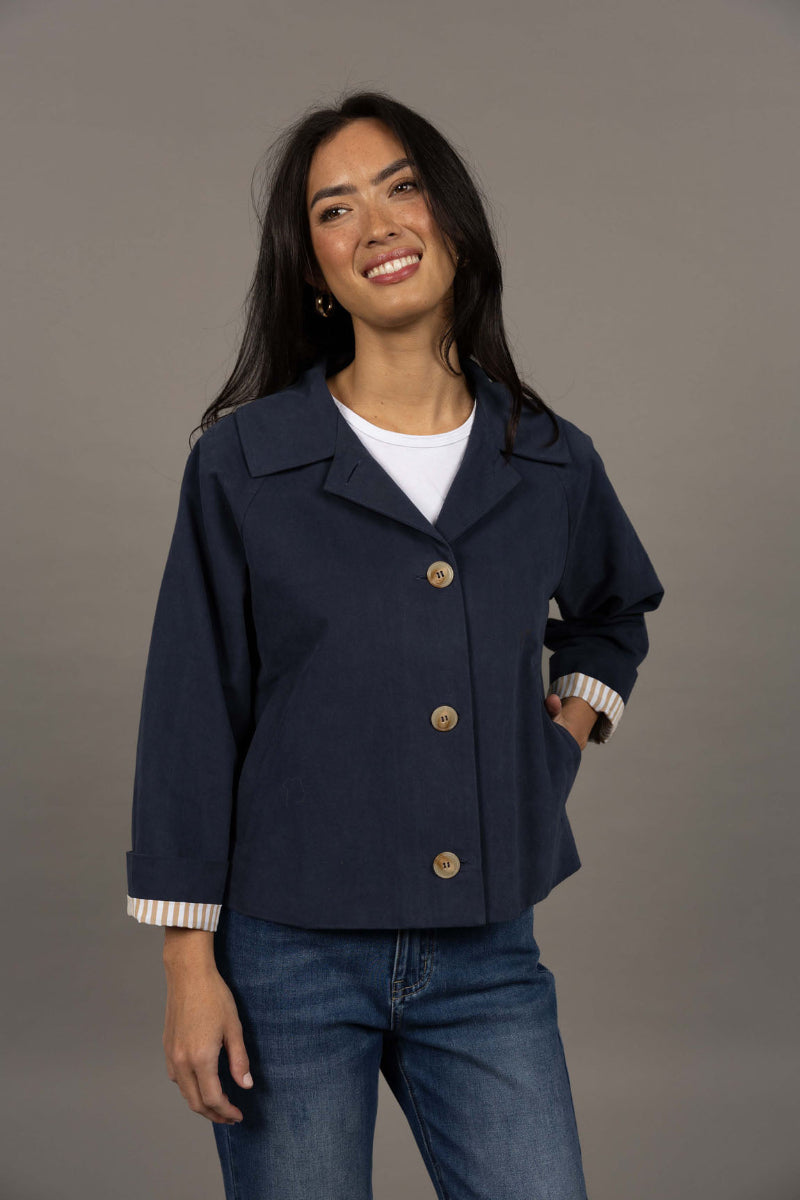 Woman wearing a navy blue jacket with gold buttons on a gray background