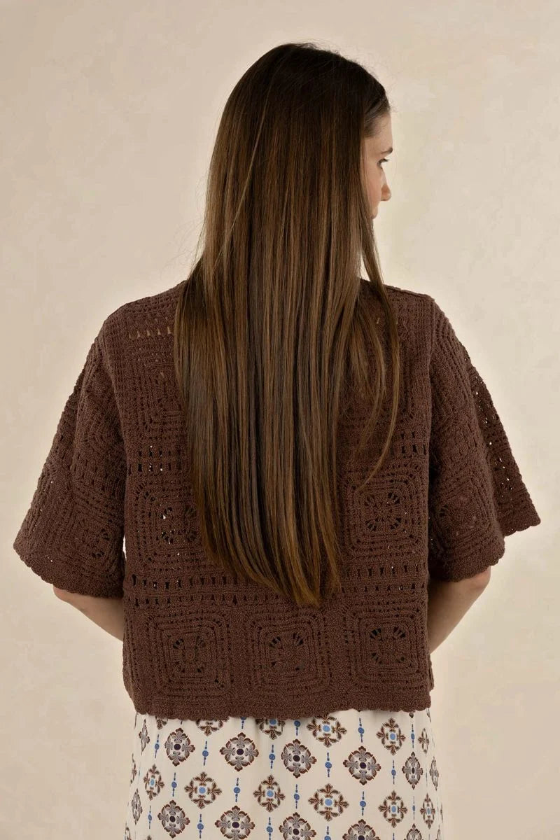 Woman wearing a brown crochet top against a beige background