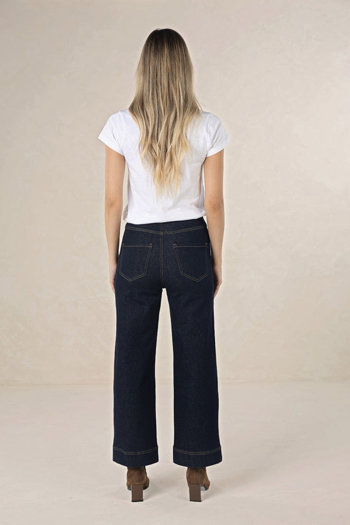 Person wearing a white t-shirt and dark jeans on a beige background