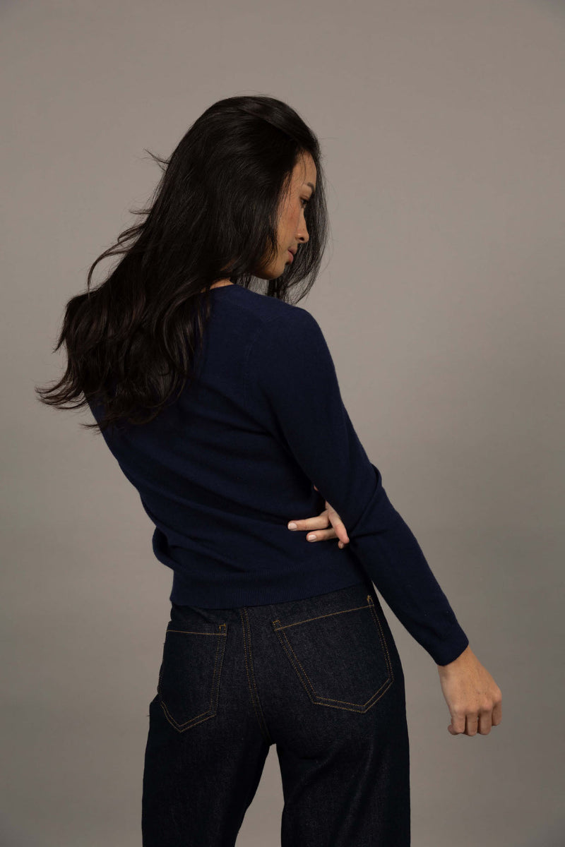 Person wearing a navy sweater and dark jeans against a gray background