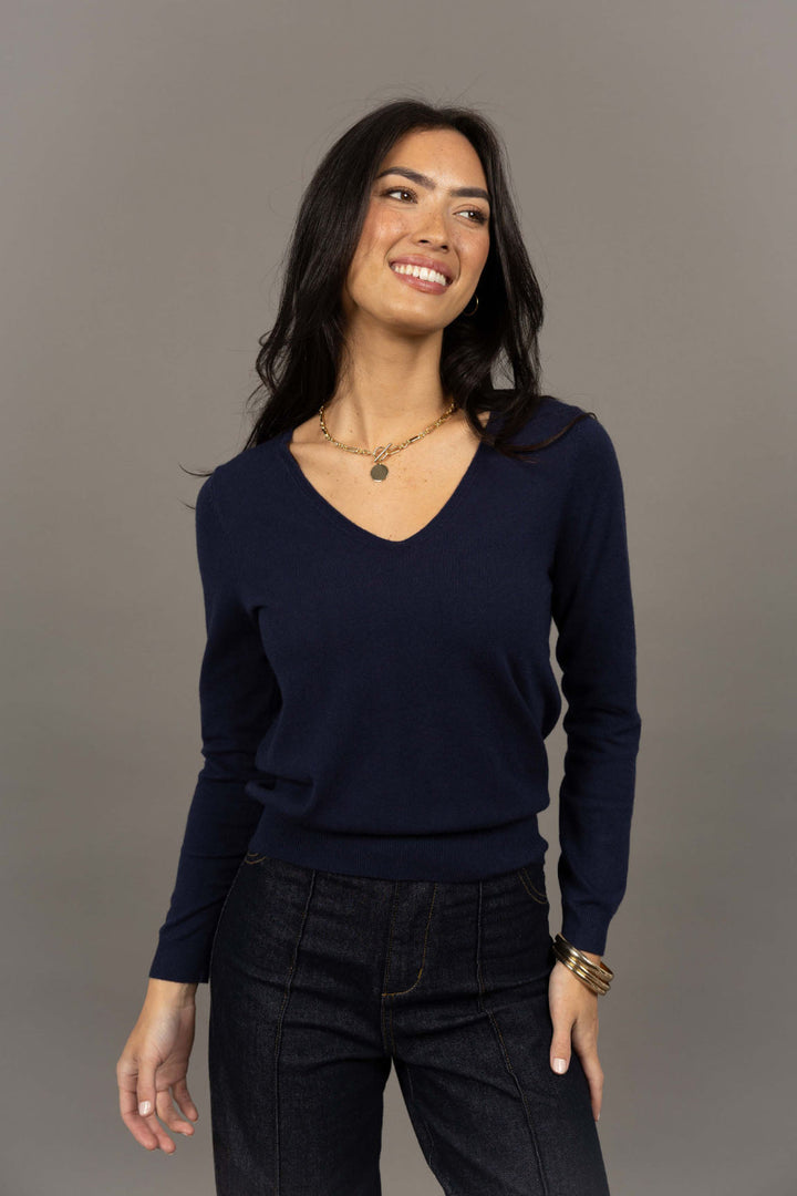 Woman wearing a navy blue sweater and black pants against a gray background
