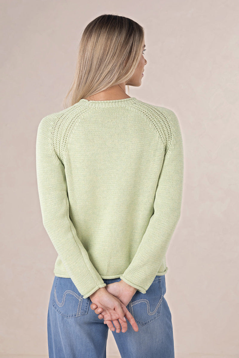 Woman wearing a light green sweater and blue jeans against a beige background