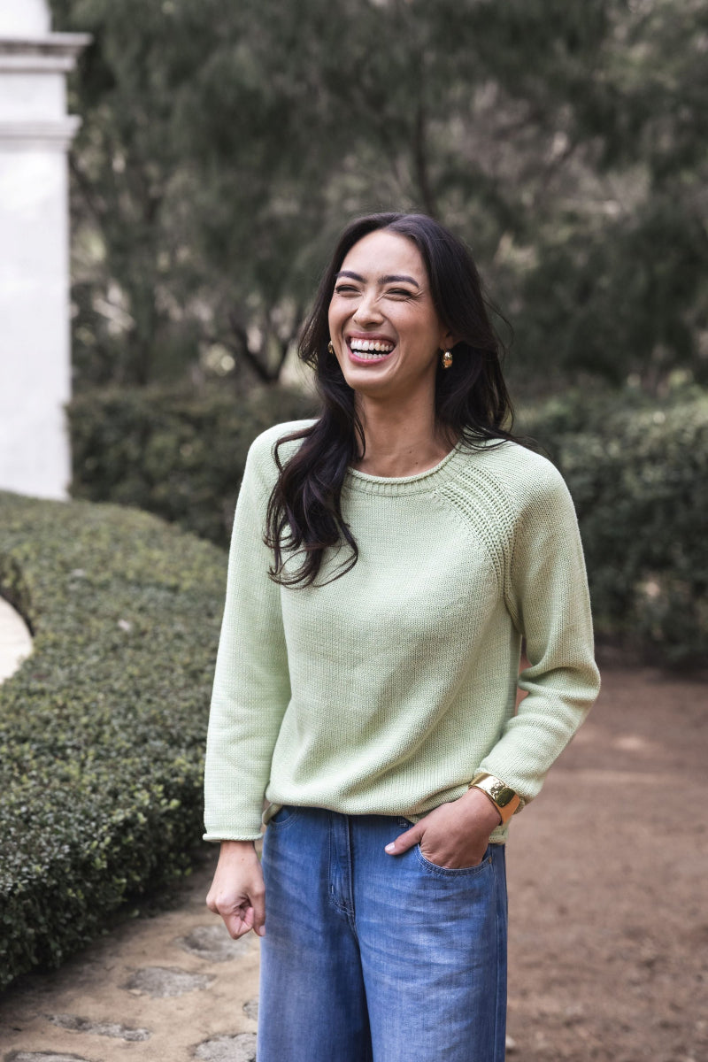 Woman wearing a light green sweater and blue jeans standing outdoors.