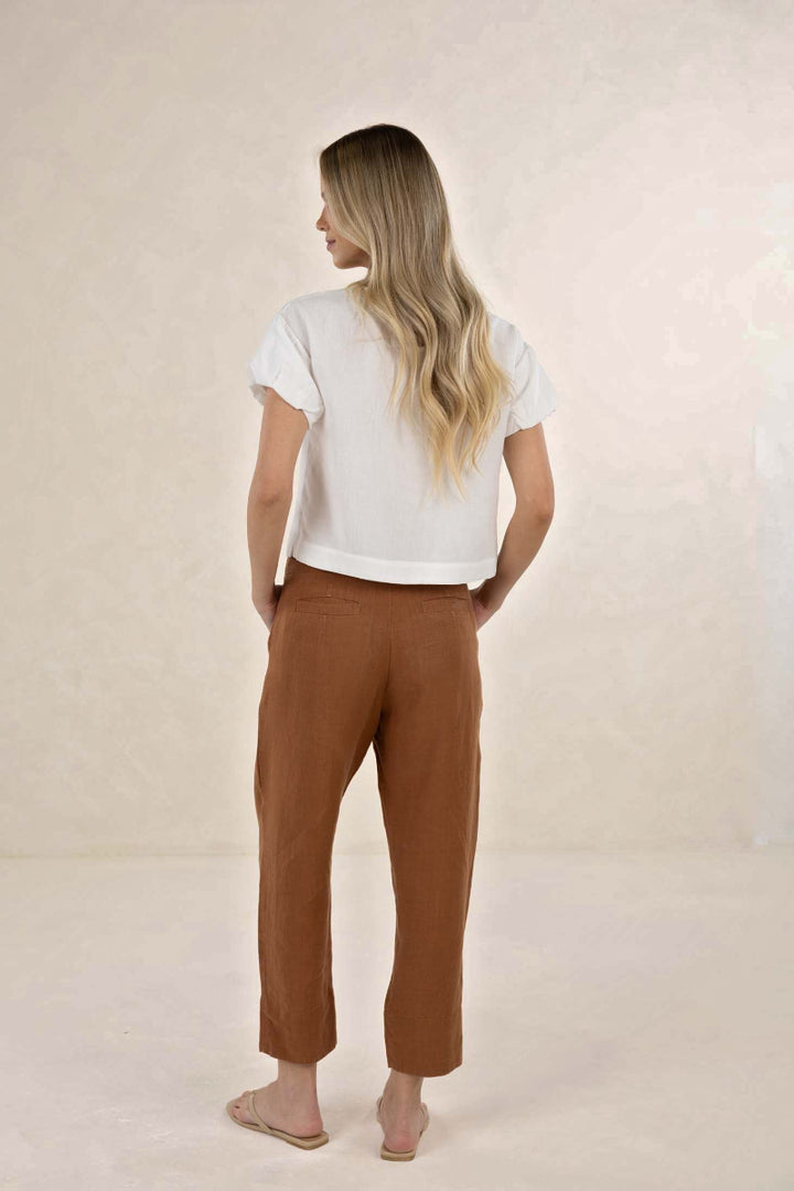 Woman wearing a white top and brown pants on a beige background