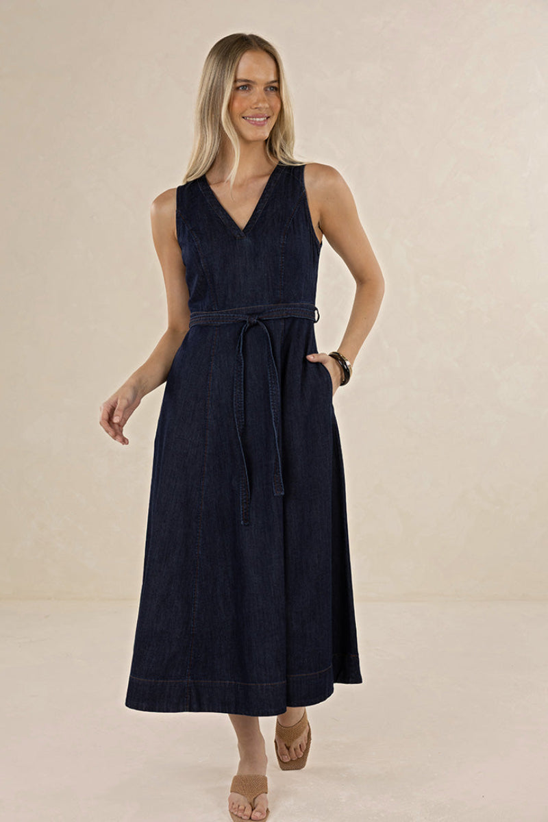 A woman modeling a sleeveless navy blue midi dress with a V-neckline, side pockets, and a matching waist tie, set against a neutral beige studio background.