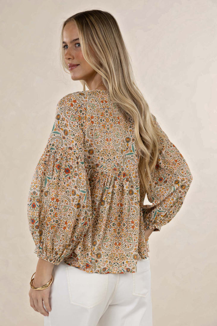 Woman wearing a floral blouse with long sleeves on a beige background