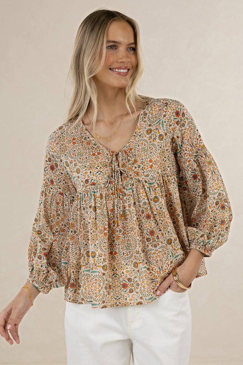 Woman wearing a patterned blouse with long sleeves on a beige background
