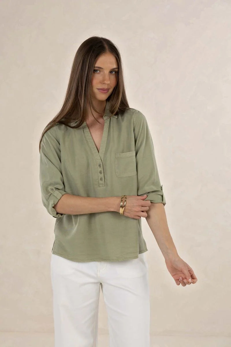 Woman wearing a green shirt and white pants against a beige background