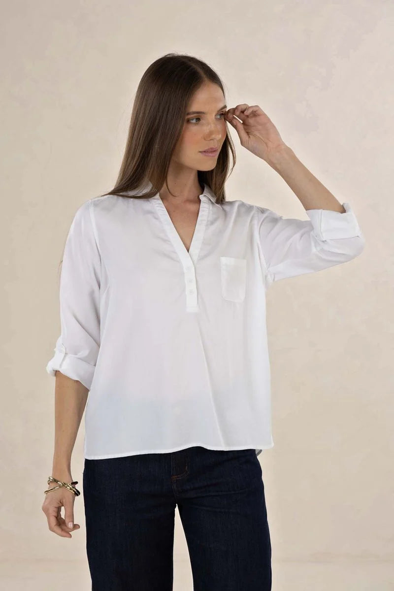 Woman wearing a white blouse and dark jeans against a beige background
