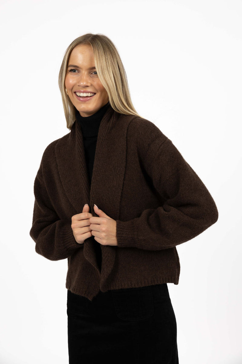 Woman wearing a brown cardigan over a black turtleneck on a white background