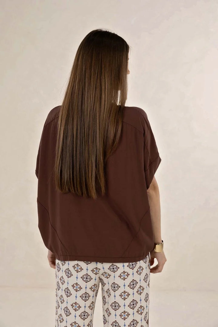 Woman wearing a brown top and patterned pants against a plain background
