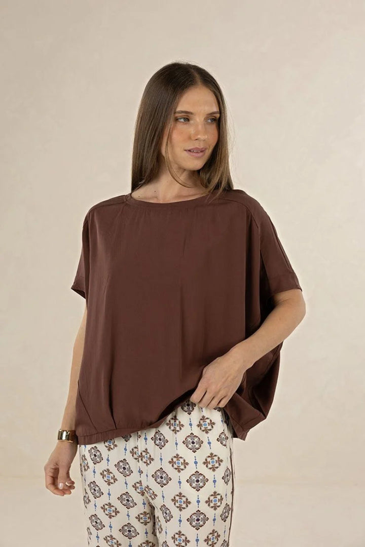 Woman wearing a brown top and patterned pants against a beige background