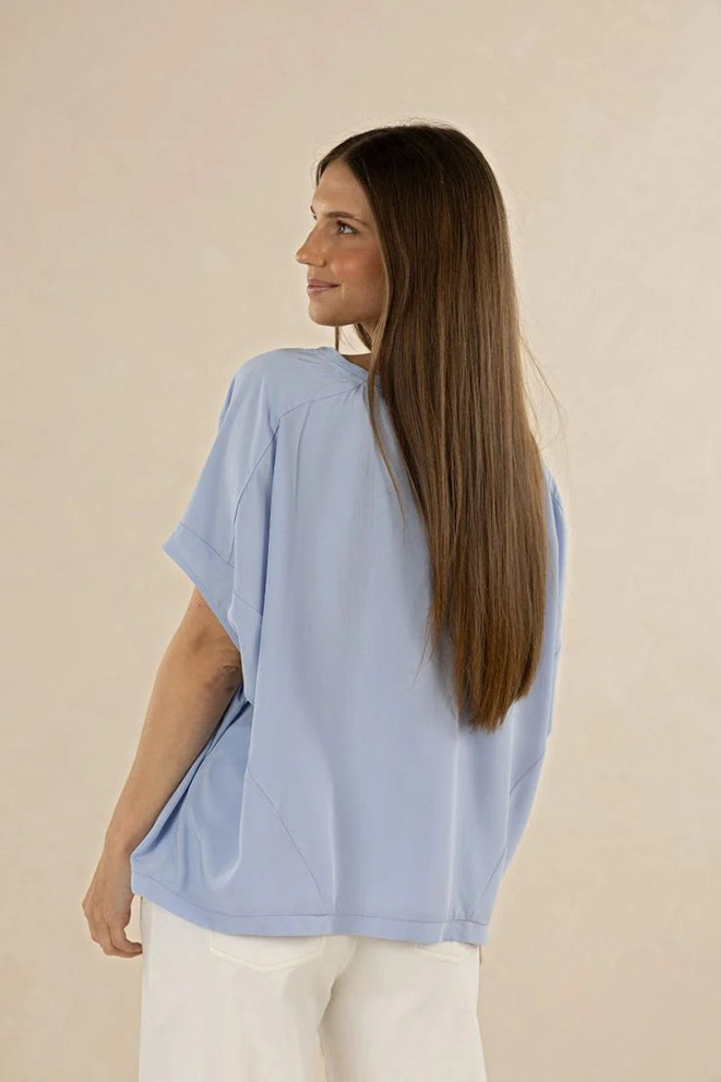 Woman wearing a light blue top and white pants against a beige background
