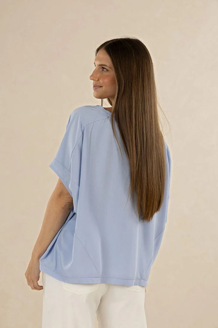 Woman wearing a light blue top and white pants against a beige background