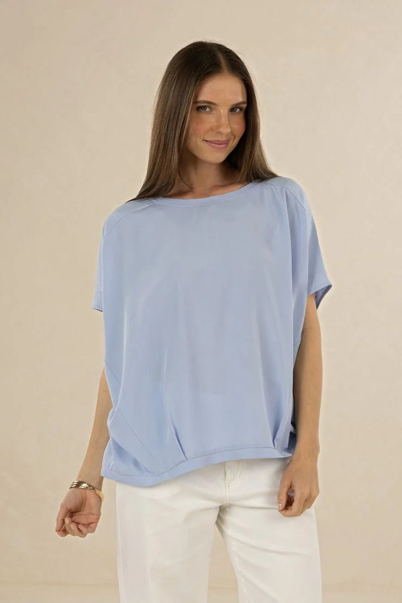 Woman wearing a light blue top and white pants on a beige background