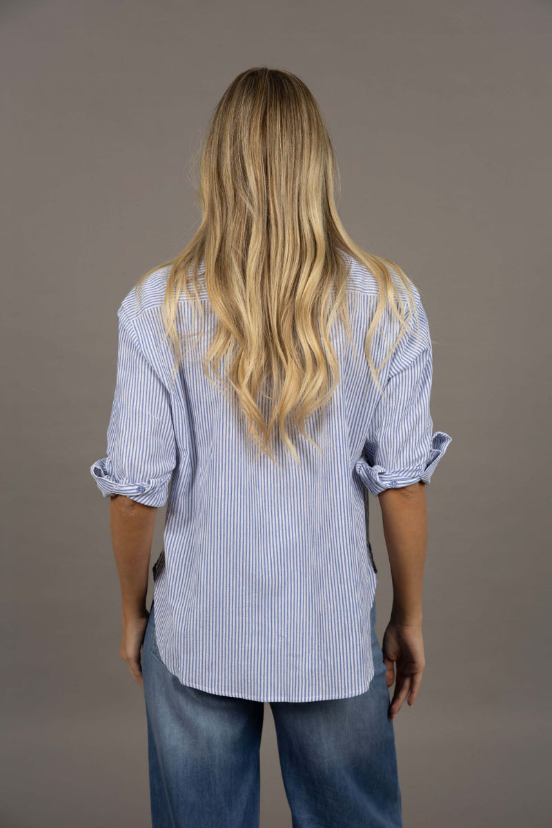 Person wearing a blue striped shirt and jeans from behind on a gray background