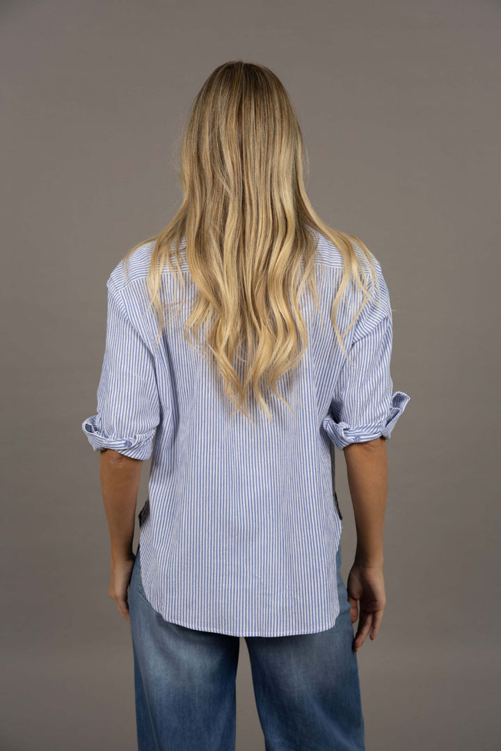 Person wearing a blue striped shirt and jeans from behind on a gray background